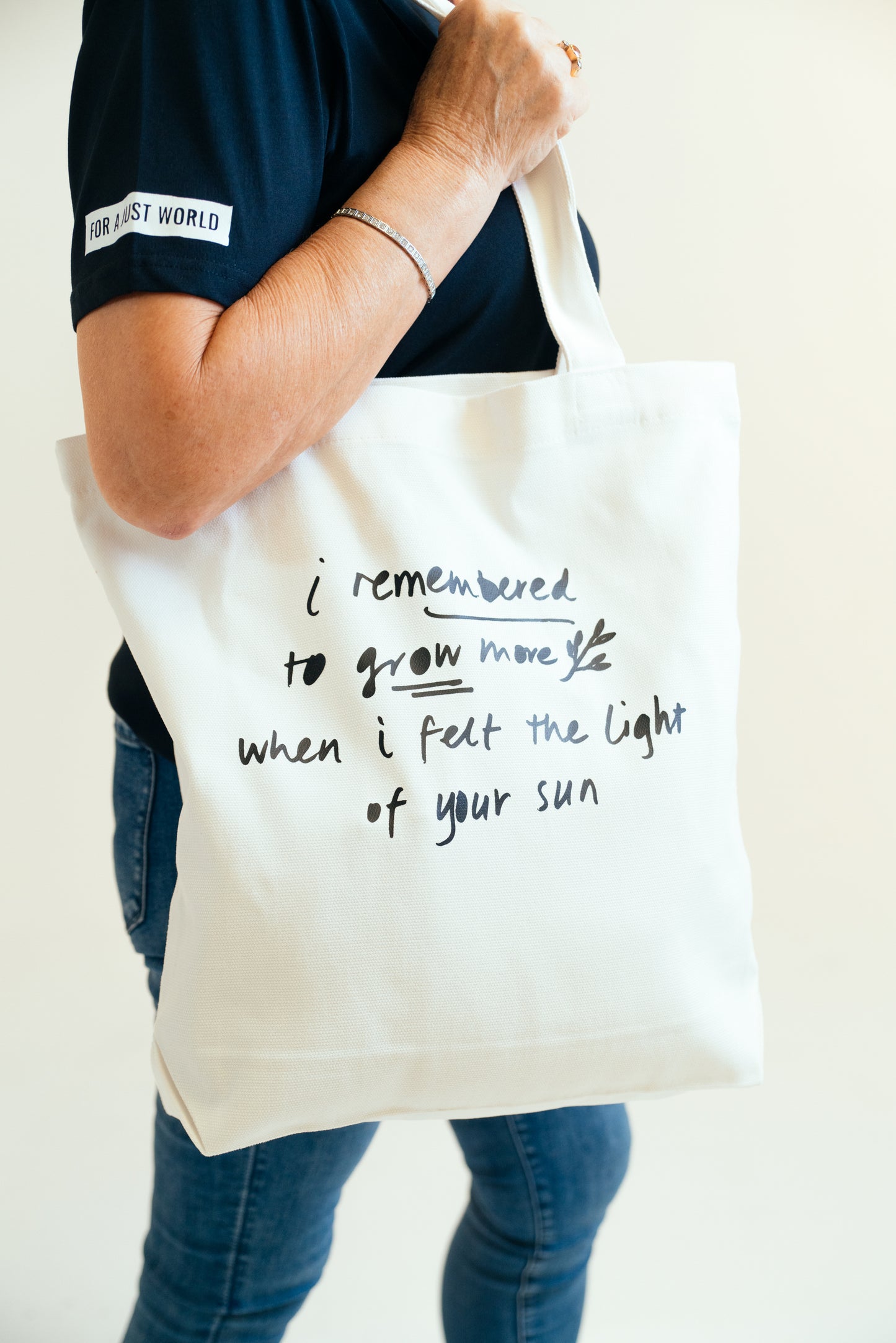 Kav Temperley tote Woman holding cream tote bag with words 'I remembered to grow more when I felt the light of your sun' in ink navy.