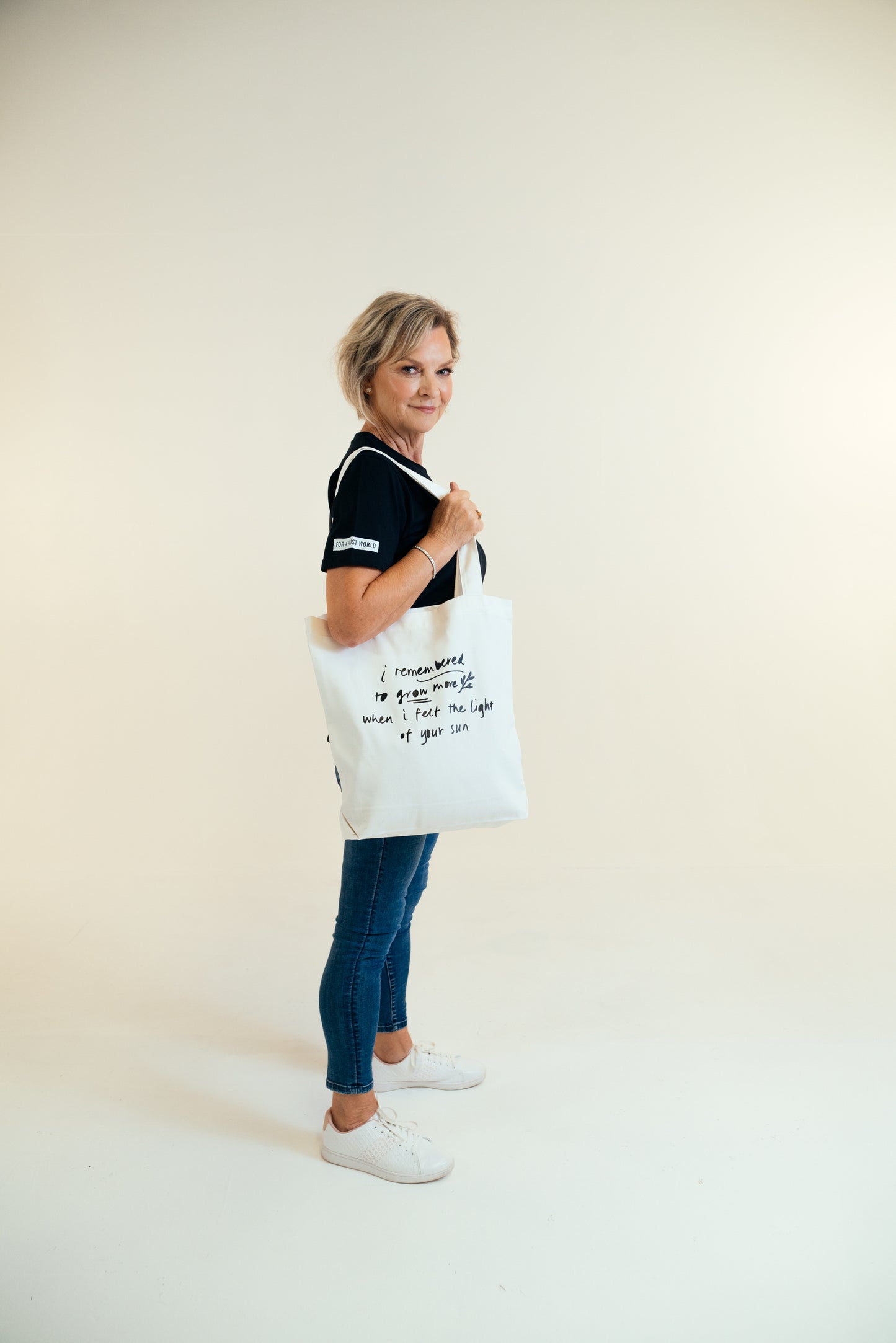 Kav Temperley tote Jenny holding cream tote bag looking at camera. Tote bag reads 'I remembered to grow more when I felt the light of you sun' in ink navy.