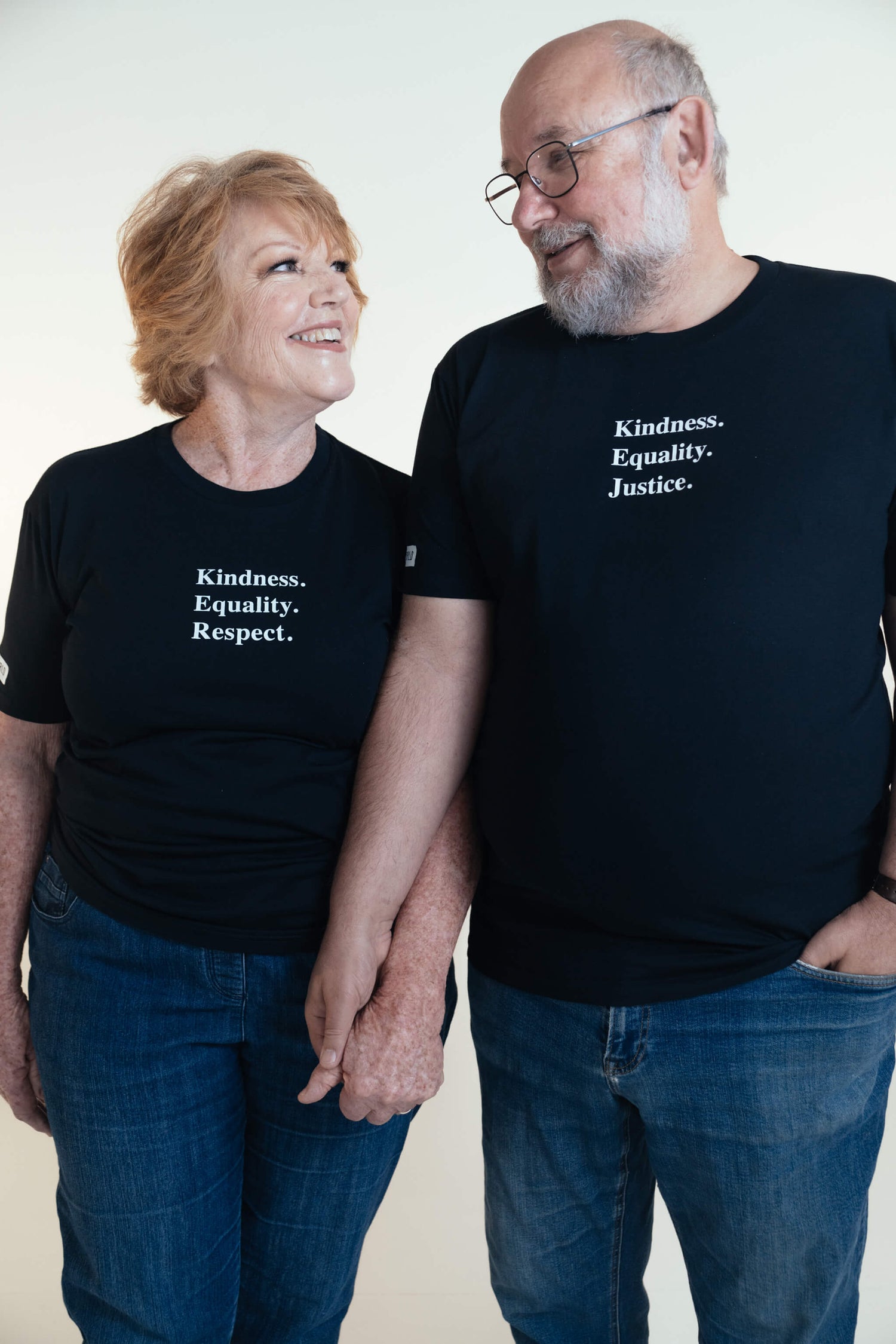 Sue holding hands with partner Steve, who is wearing an ink blue tshirt with the words 'Kindness Equality Justice.' written in white.