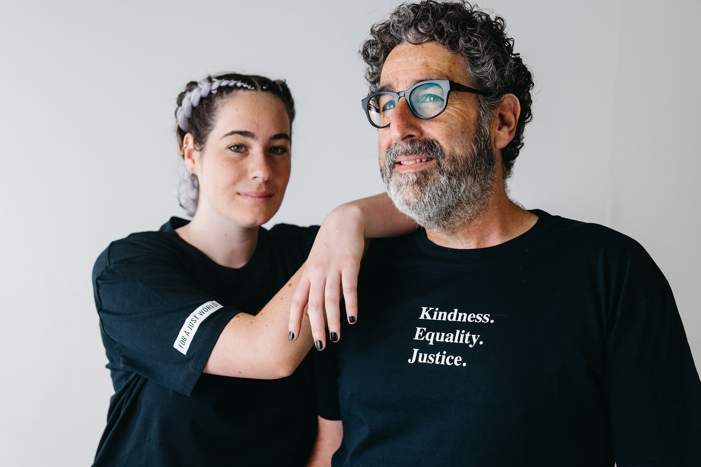 Sofia leaning on Joe's shoulder. Joe is looking into the distance wearing an ink blue tshirt with the words 'Kindness Equality Justice.' written in white.