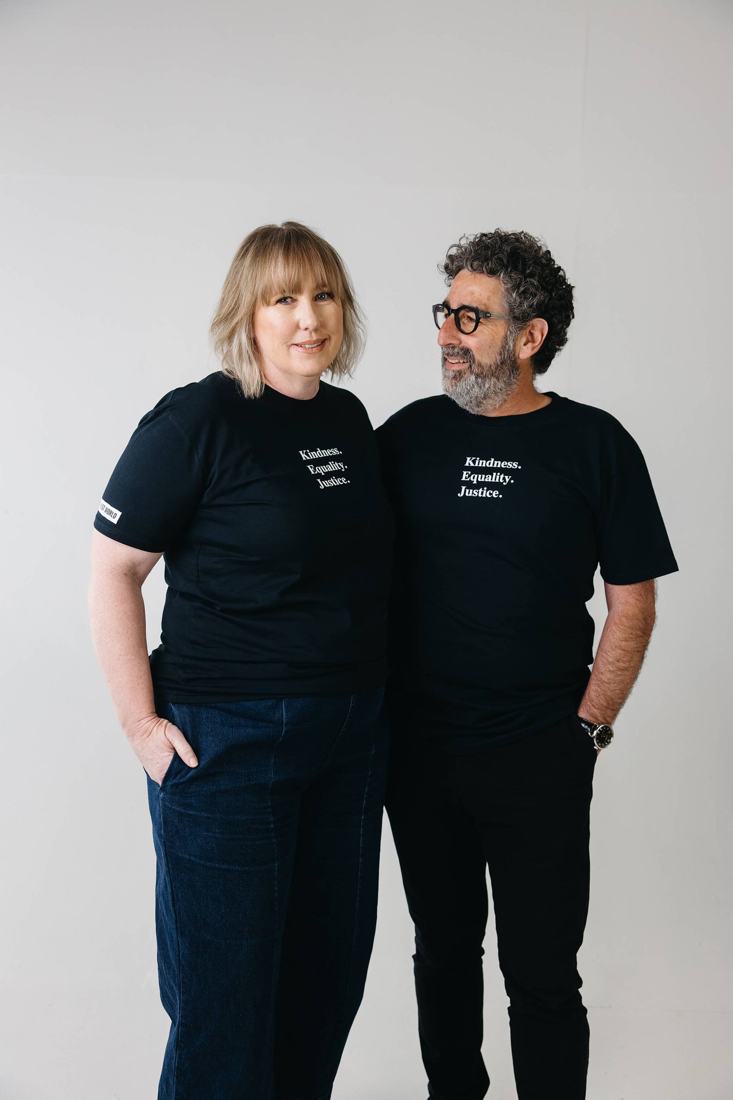 Mel and Joe smiling, both wearing wearing ink blue tshirts with the words 'Kindness Equality Justice.' written in white.