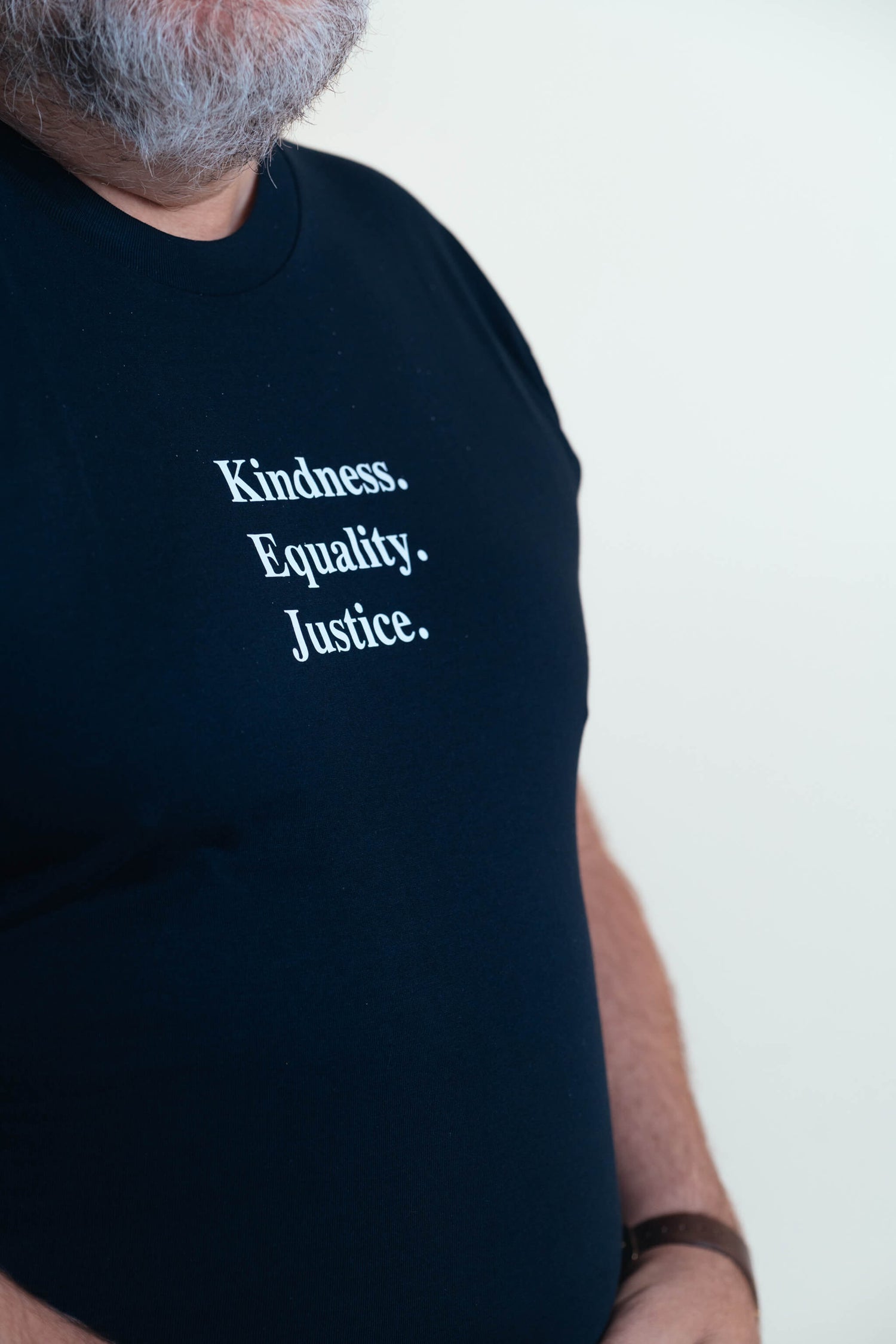 Close up on Steve wearing an ink blue tshirt with the words 'Kindness Equality Justice.' written in white.