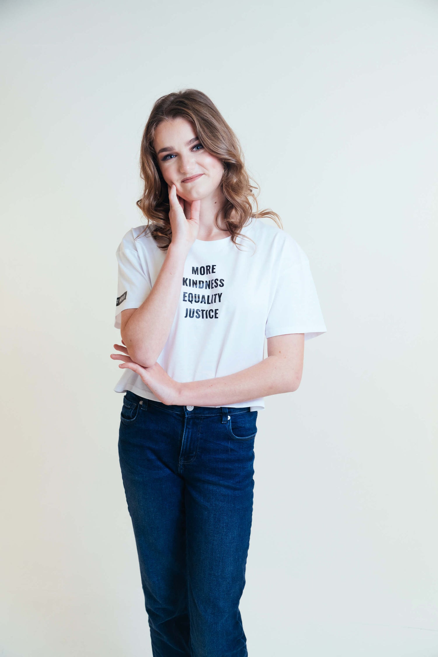 Angie smiling at the camera wearing a white crop top with the words 'More Kindness Equality Justice' written in black.